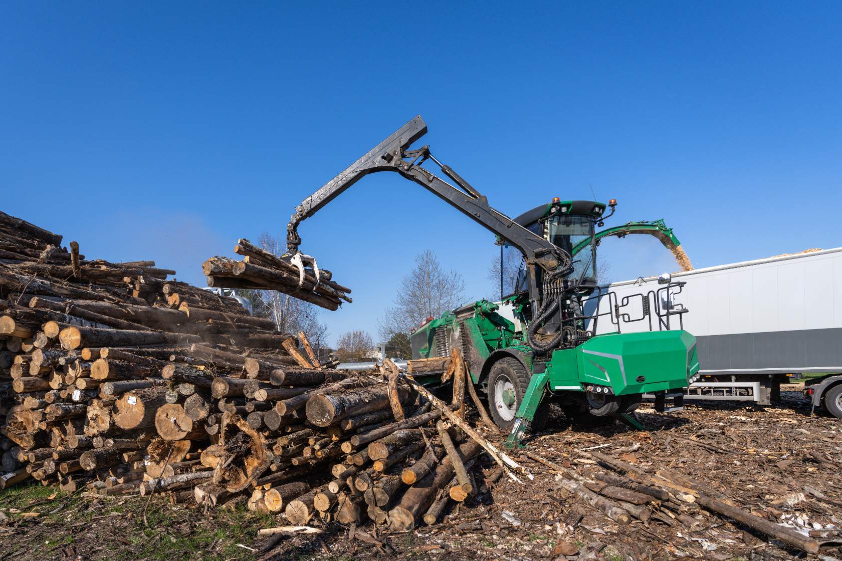 A green tractor with a pile of logs in front of it, ready for wood chipping.