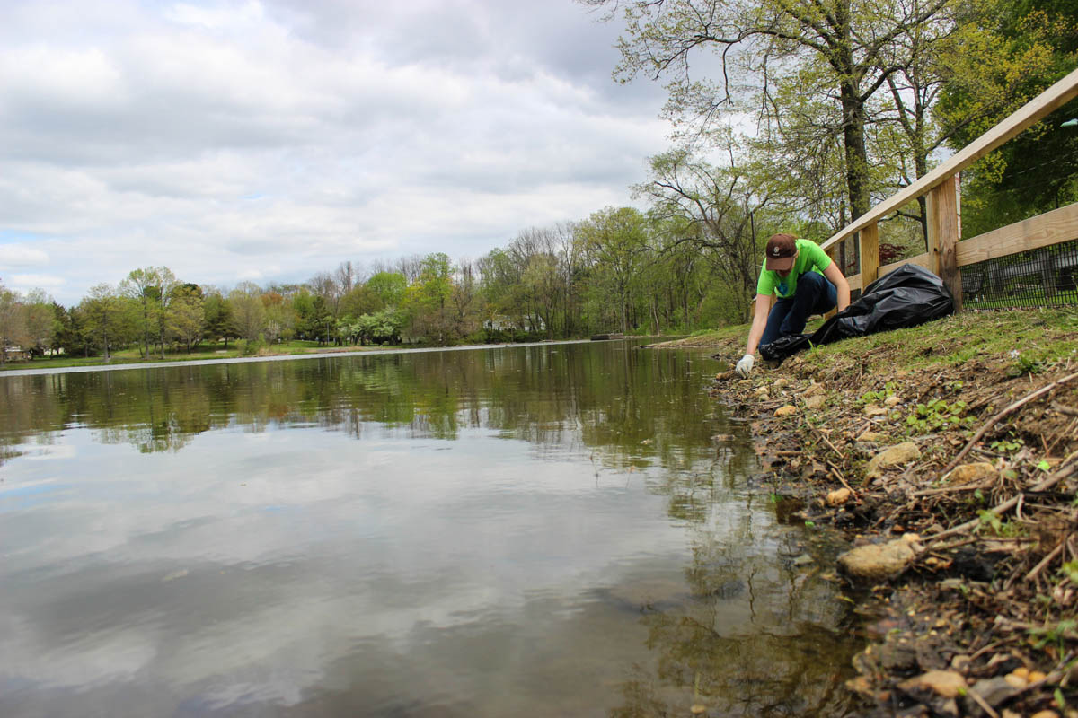 A person kneeling on the side of a pond.