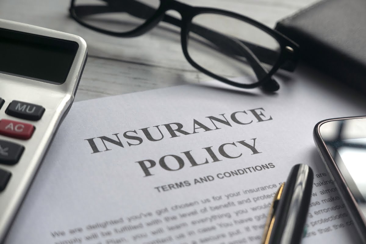 A close-up of an insurance policy document on a desk, accompanied by a calculator, eyeglasses, a pen, a smartphone, and a wallet highlights the meticulous nature often required in professional tree removal.