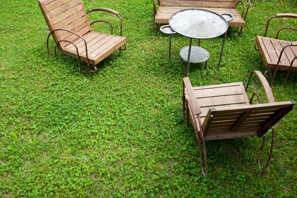 Outdoor seating area with four wooden chairs and a circular metal table set on a grassy lawn, perfect for relaxing while considering storm proofing your home.