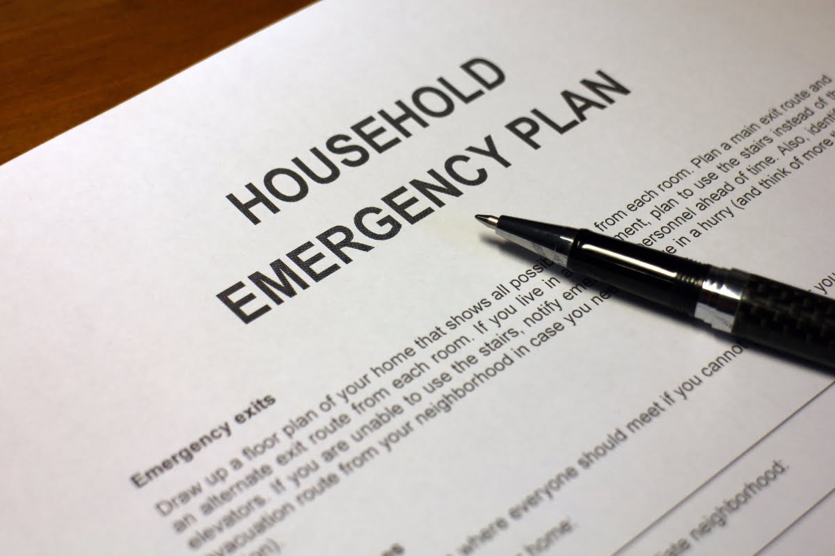 A pen lies on a printed document titled "Household Emergency Plan," detailing emergency exits, safety measures, and storm proofing your home.