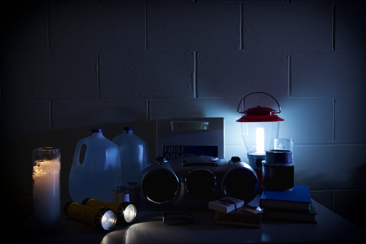 A table with emergency supplies, including flashlights, a radio, candles, jugs of water, a lantern, canned food, matches, and a first aid kit sits against a dimly lit wall—a vital setup in the wake of Georgia storm damage.