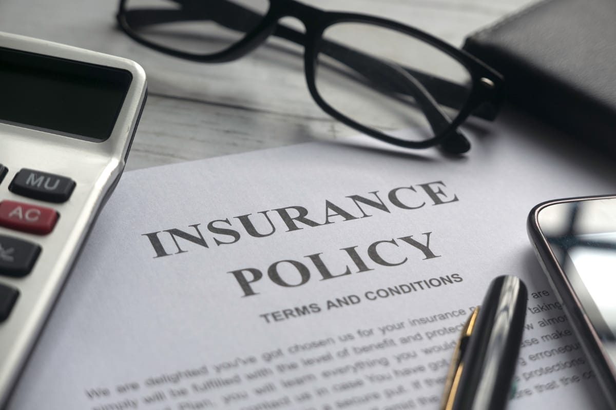 A close-up of an insurance policy document on a desk, flanked by a calculator, glasses, a pen, and a smartphone—essential tools for navigating storm damage insurance claims.